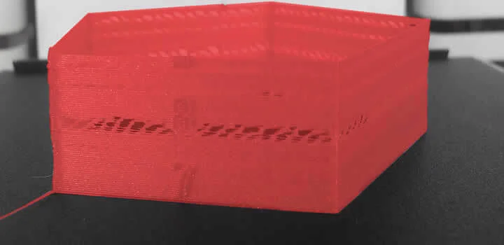peça vermelha com problema aparente de sub-extrusão e camadas faltando ou falhando em cima de uma mesa preta feita em impressora 3d com filamento 3d