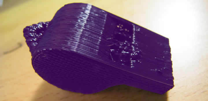 Foto de um apito impresso com filamento abs roxo com sobre-extrusão em cima de uma mesa de madeira